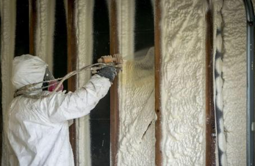 A worker insulating the wall of a garage with spray foam insulation.