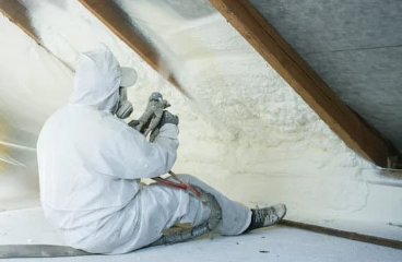 Technician applying spray polyurethane foam insulation to an attic using a plural component gun.